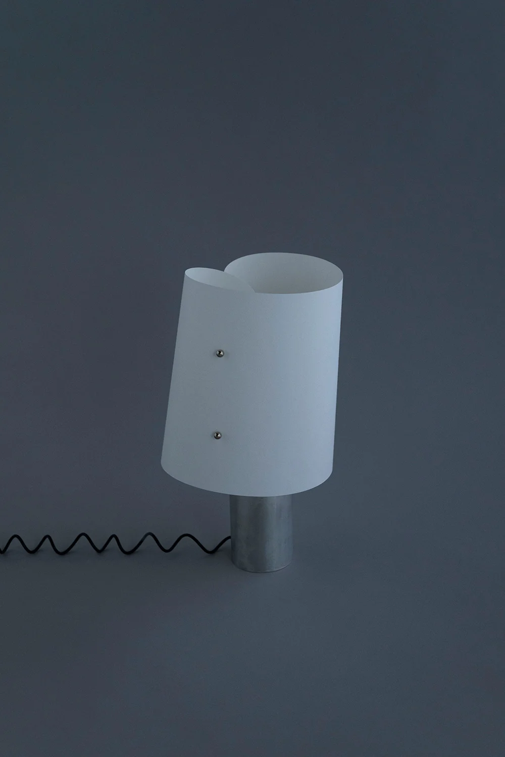 Curly seen from the side, the paper shade leaning on its aluminum base